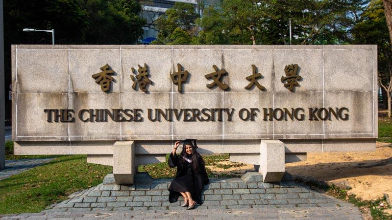 Student sitting at The Chinese University of Hong Kong campus sign showcasing CUHK campus environment and student life